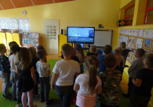Grupa dzieci stoi na przeciwko ekranu mobilnego i ogląda start rakiety.